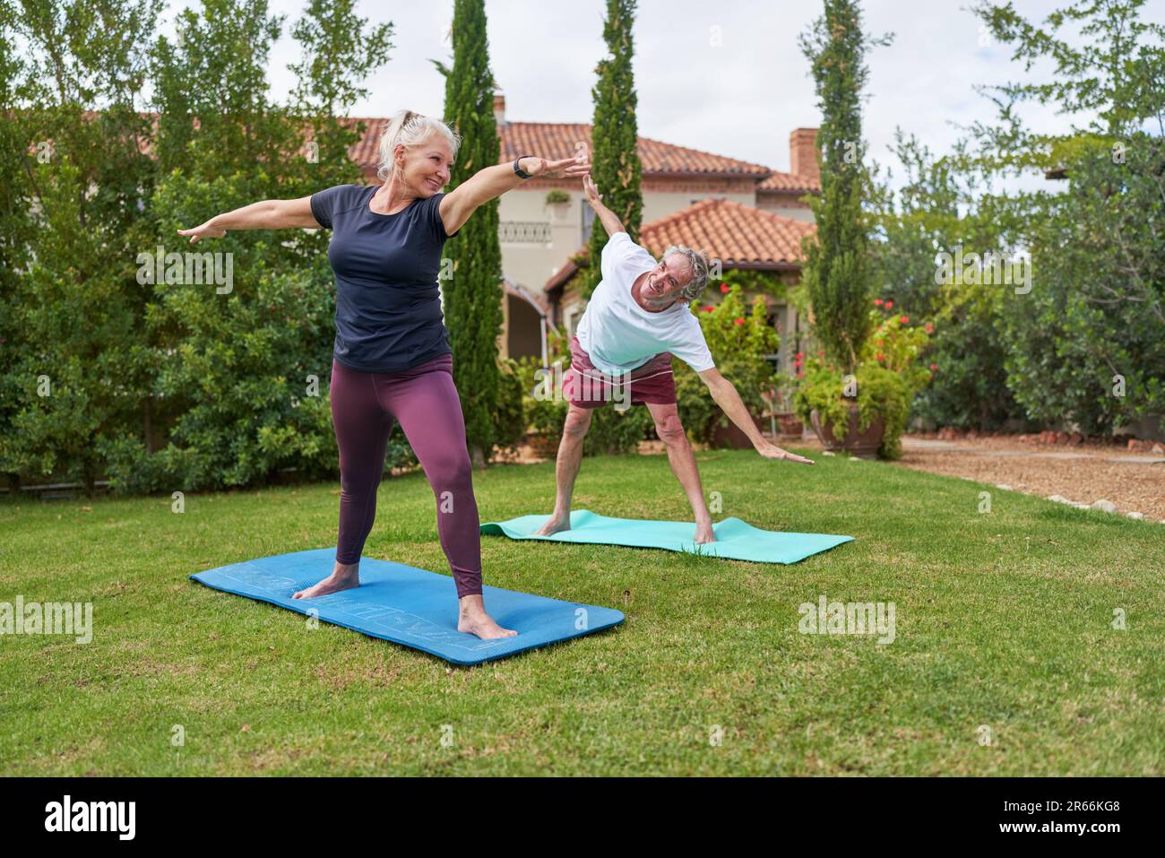 Glückliches, aktives Seniorenpaar, das Yoga im Villengarten praktiziert Stockfoto