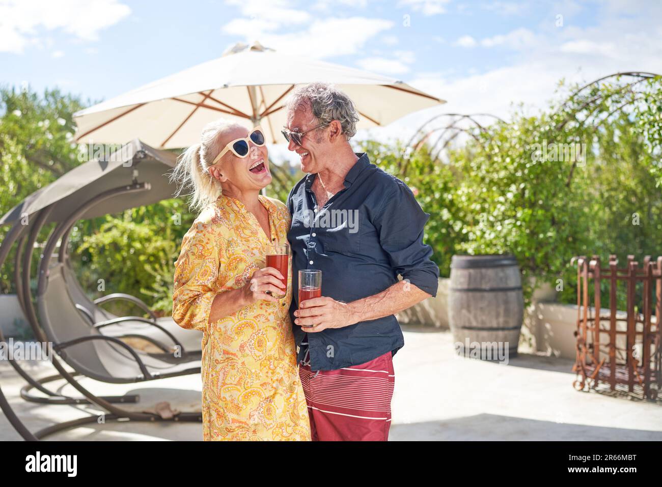 Glückliches Seniorenpaar, das lacht und Cocktails auf der Sommerterrasse trinkt Stockfoto