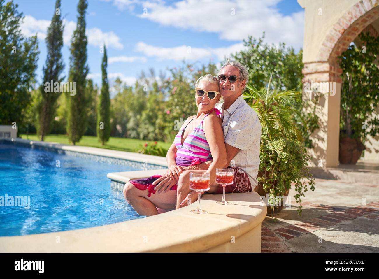 Portrait glückliches Seniorenpaar, das sich im sonnigen Sommerschwimmbad entspannt Stockfoto