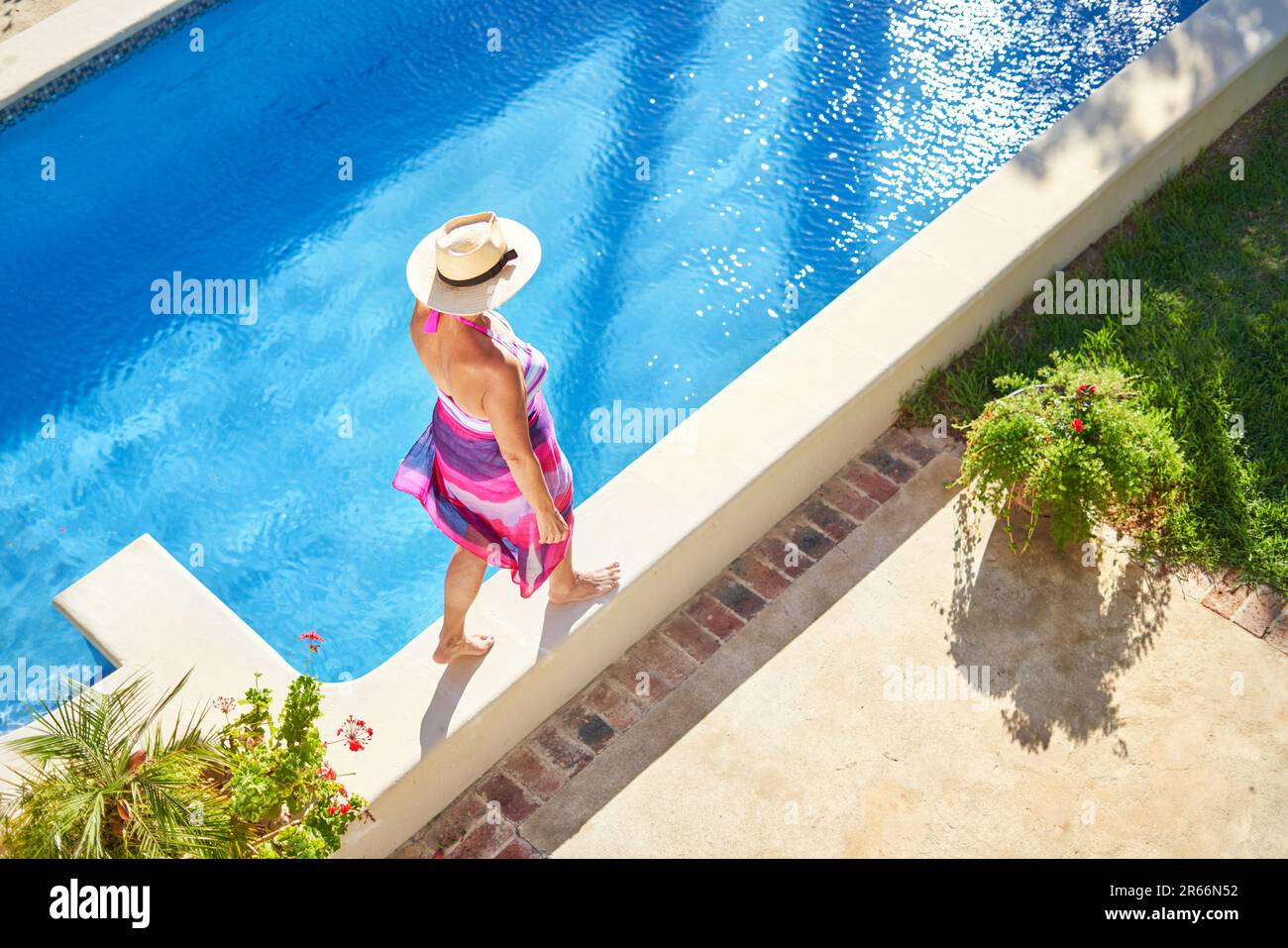 Frau mit Strohhut, die am Rand des sonnigen Swimmingpools spaziert Stockfoto