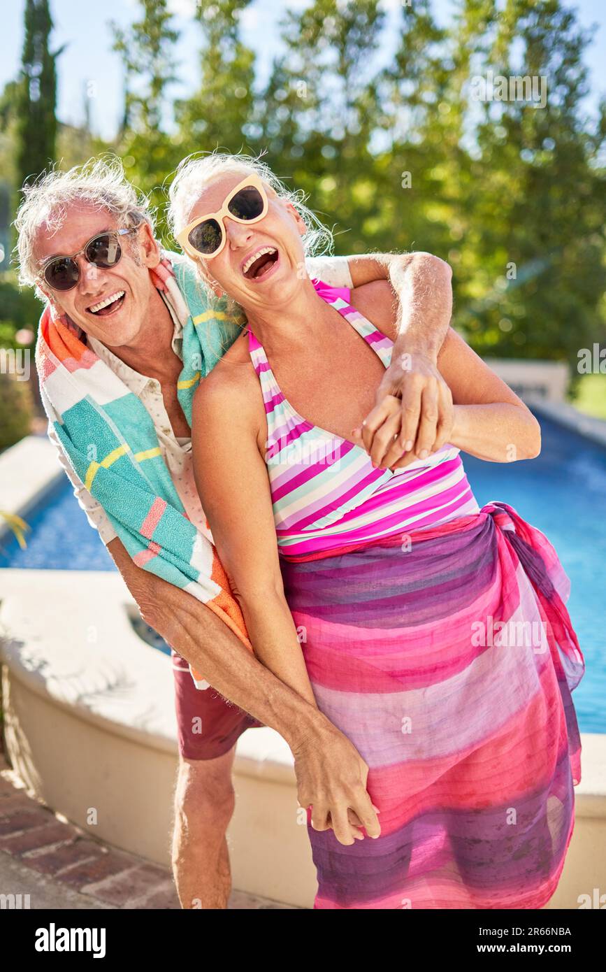 Porträt fröhliches, verspieltes Seniorenpaar, das sich am sonnigen Pool umarmt Stockfoto