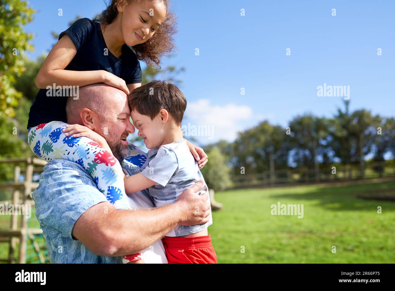 Vater hält, trägt Tochter und Sohn mit Down-Syndrom im Park Stockfoto