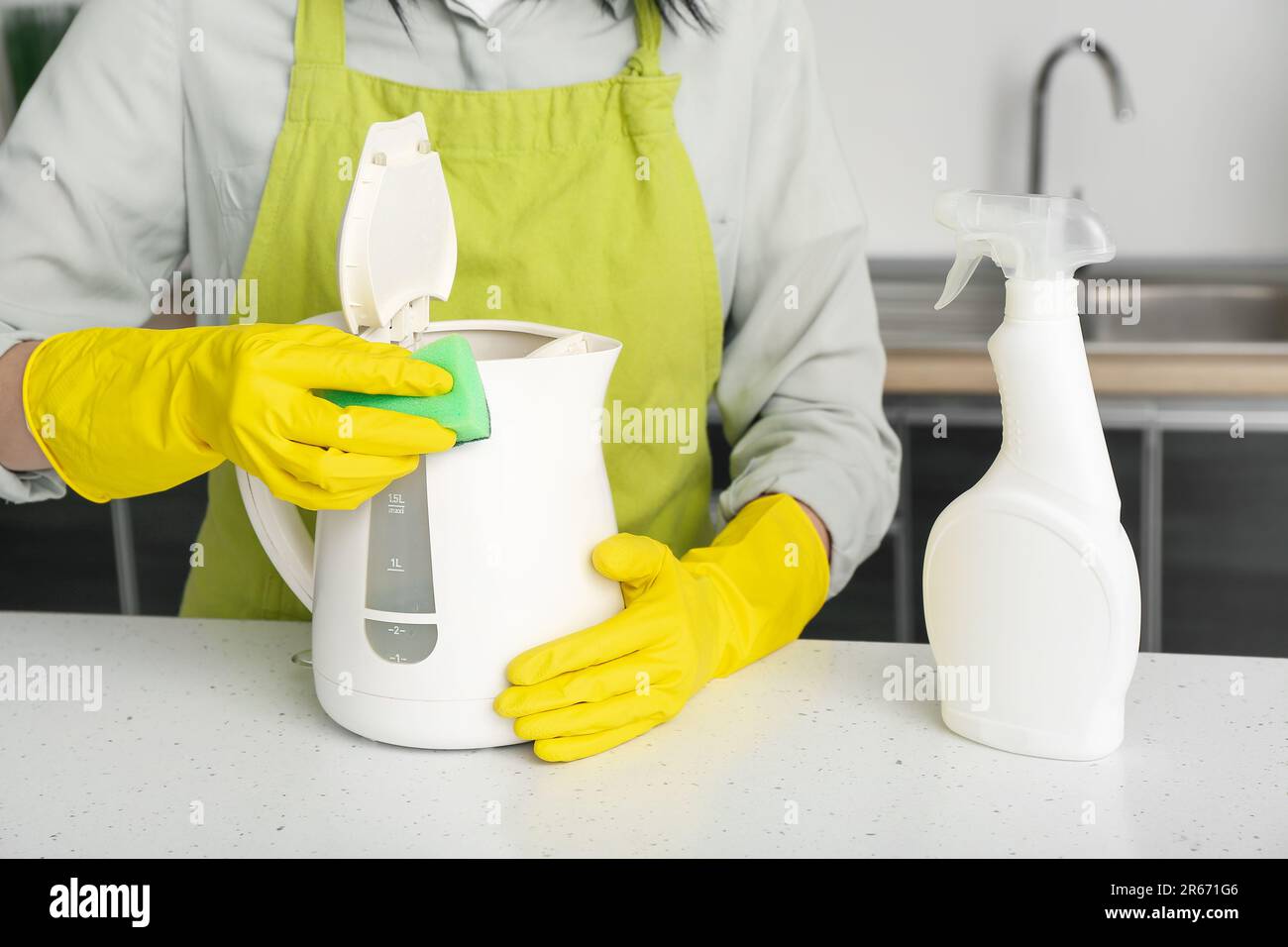 Frau in gelben Handschuhen, die elektrischen Wasserkocher auf einem weißen Tisch reinigt Stockfoto