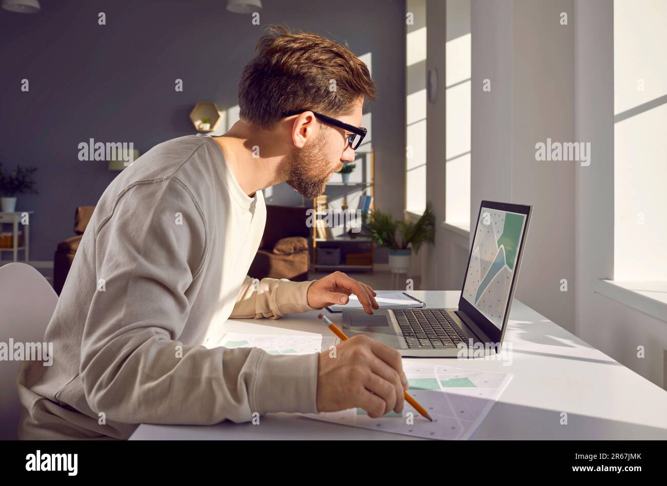 Mann, der seinen Laptop benutzt, während er mit digitalen und papierbasierten Stadtplänen arbeitet Stockfoto