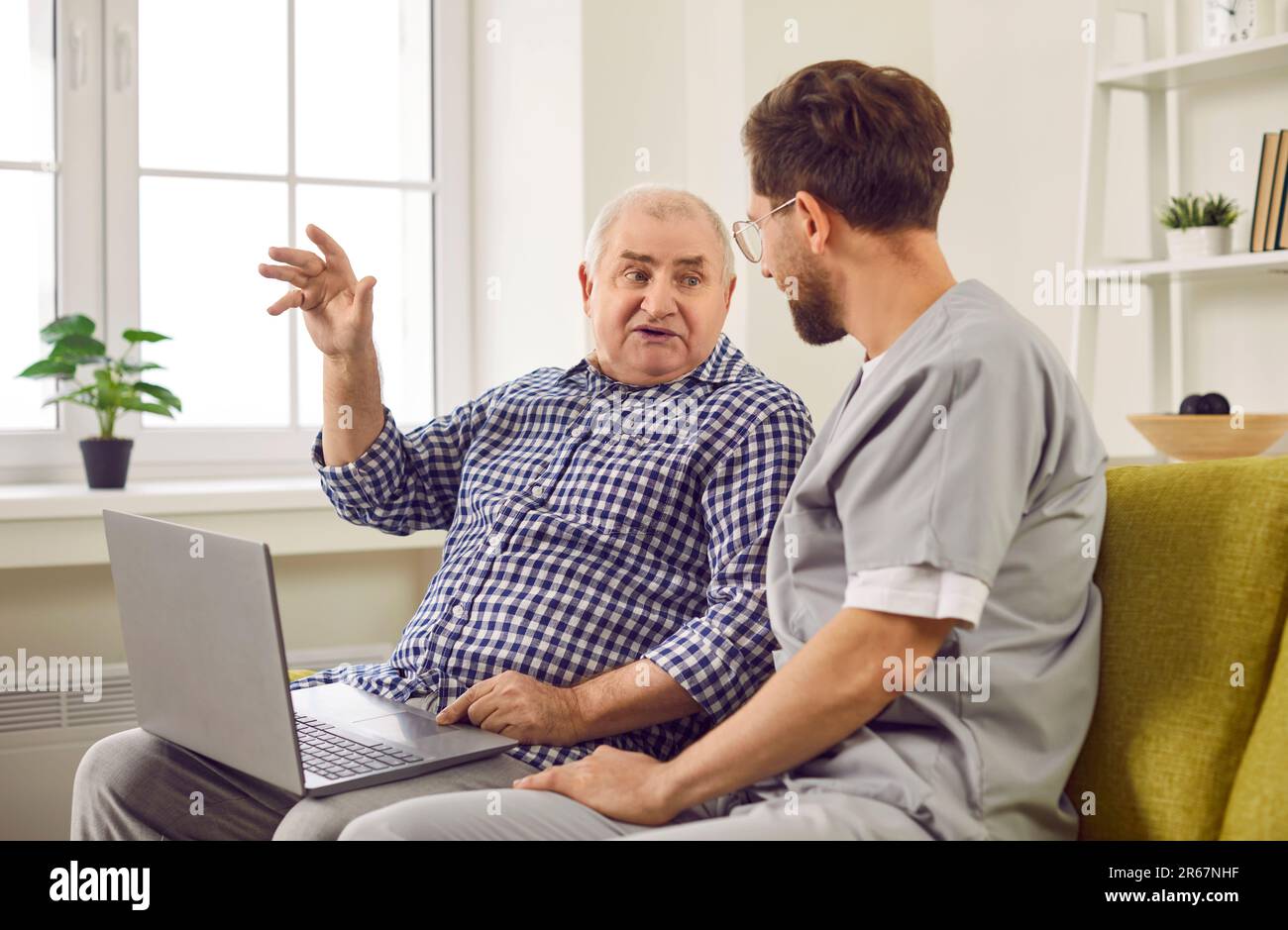 Freundlicher junger Krankenpfleger, der Seniorin bei der Verwendung des Laptops zu Hause hilft. Stockfoto