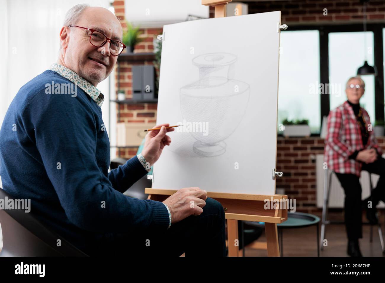 Glücklicher Senior-Mann beim Kunstworkshop. Positiver pensionierter Schüler, der an der Staffelei sitzt und im Unterricht auf Leinwand zeichnet, und es genießt, neue Dinge zu lernen. Kreatives Altersvorsorgekonzept Stockfoto