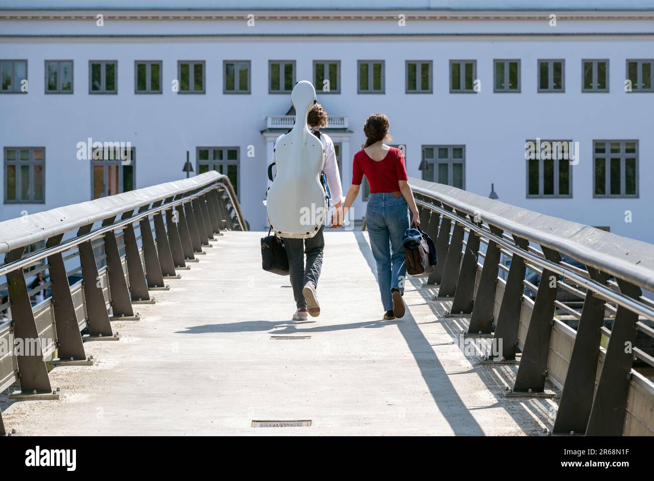 Ein junges Paar Hand in Hand von hinten, das über eine Fußgängerbrücke geht, trägt eine Cello-Box auf dem Rücken, Konzept für den Weg nach vorn mit Liebe an Stockfoto