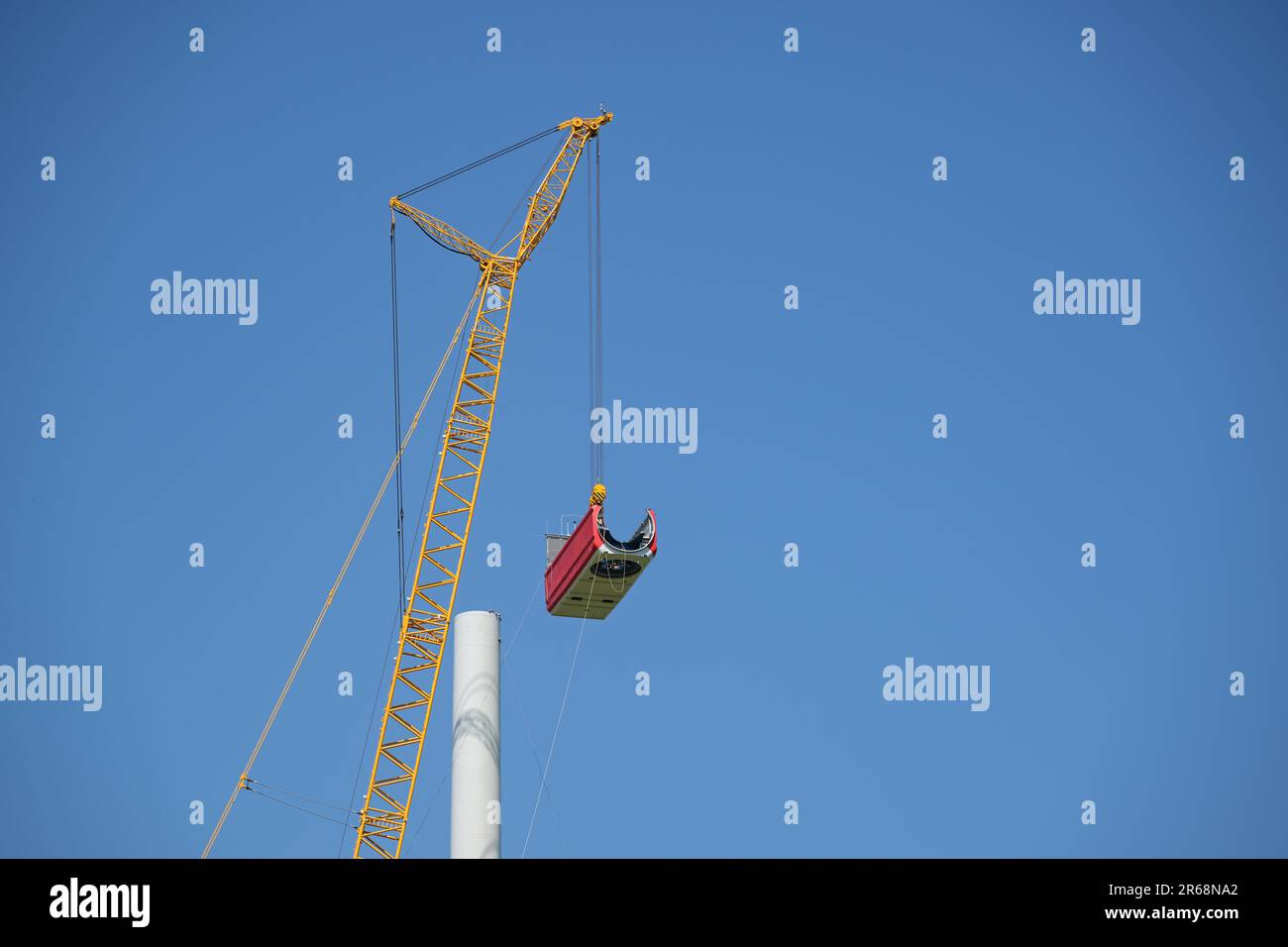 Kran, der die Gondel hebt, um sie auf dem Turm einer Windturbine auf einer Baustelle zu installieren, Elektrizität, erneuerbare Energien und Stromkonzept, blau Stockfoto