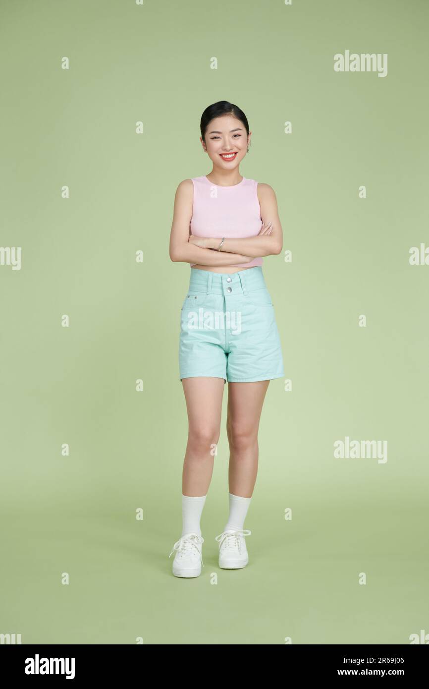 Die ganze Länge der aisan-Frau kreuzte sich die Hand und lächelte in trendigen Kleidern, isoliert auf hellgrünem Hintergrund Stockfoto