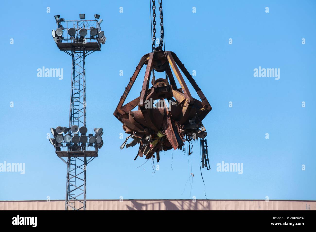 Der hydraulische Greifer transportiert rostigen Metallschrott zum Recycling unter klarem blauen Himmel an einem sonnigen Tag Stockfoto