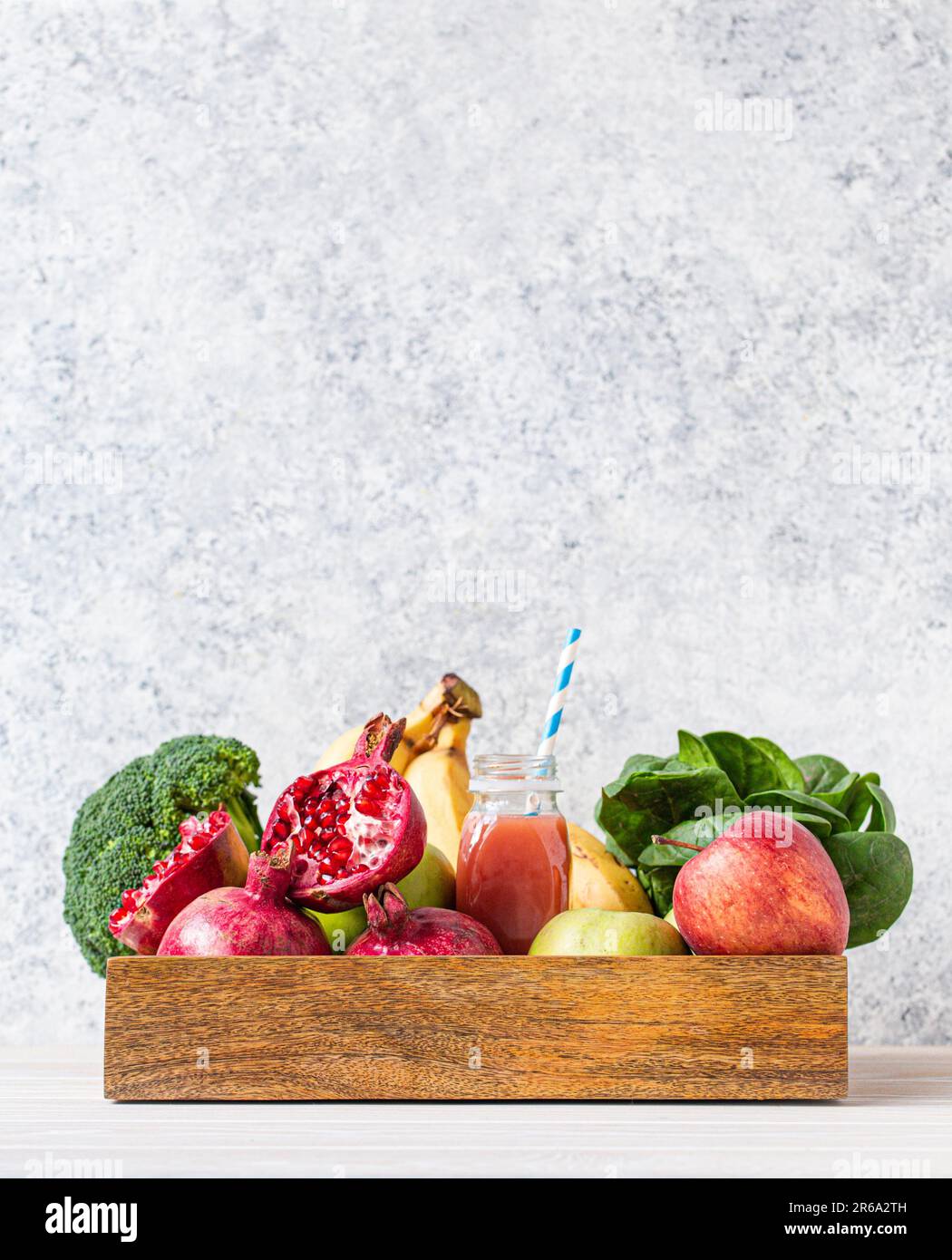 Obst, Gemüse, Gemüse in einer Holzschale und frischer Smoothie oder Saft in der Flasche mit Papierstroh auf dem Tisch nahe der weißen Wand, Entgiftung, Diät, sauberes Essen Stockfoto