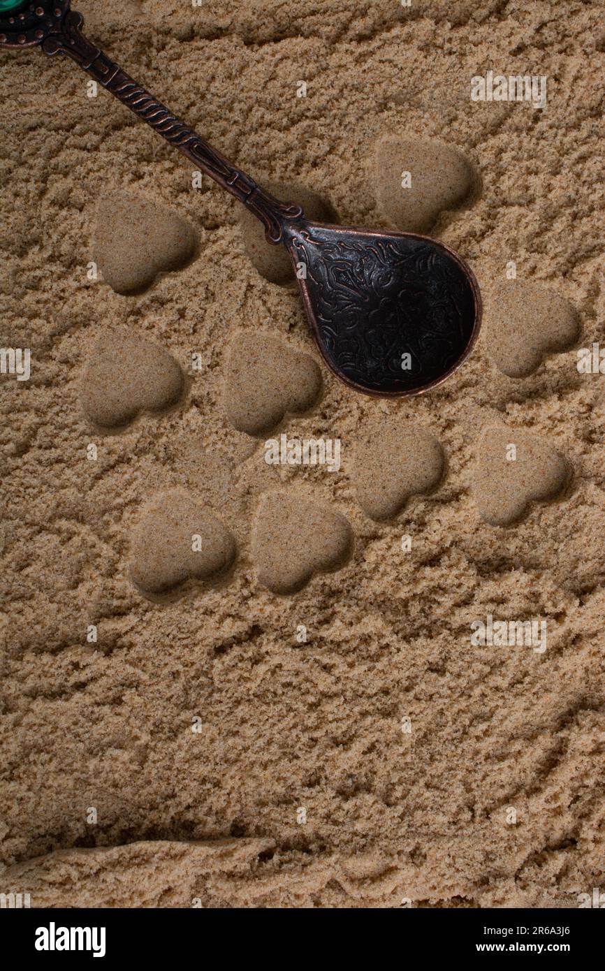 Herz Formen auf dem Sand Hintergrund neben einem Teelöffel Stockfoto