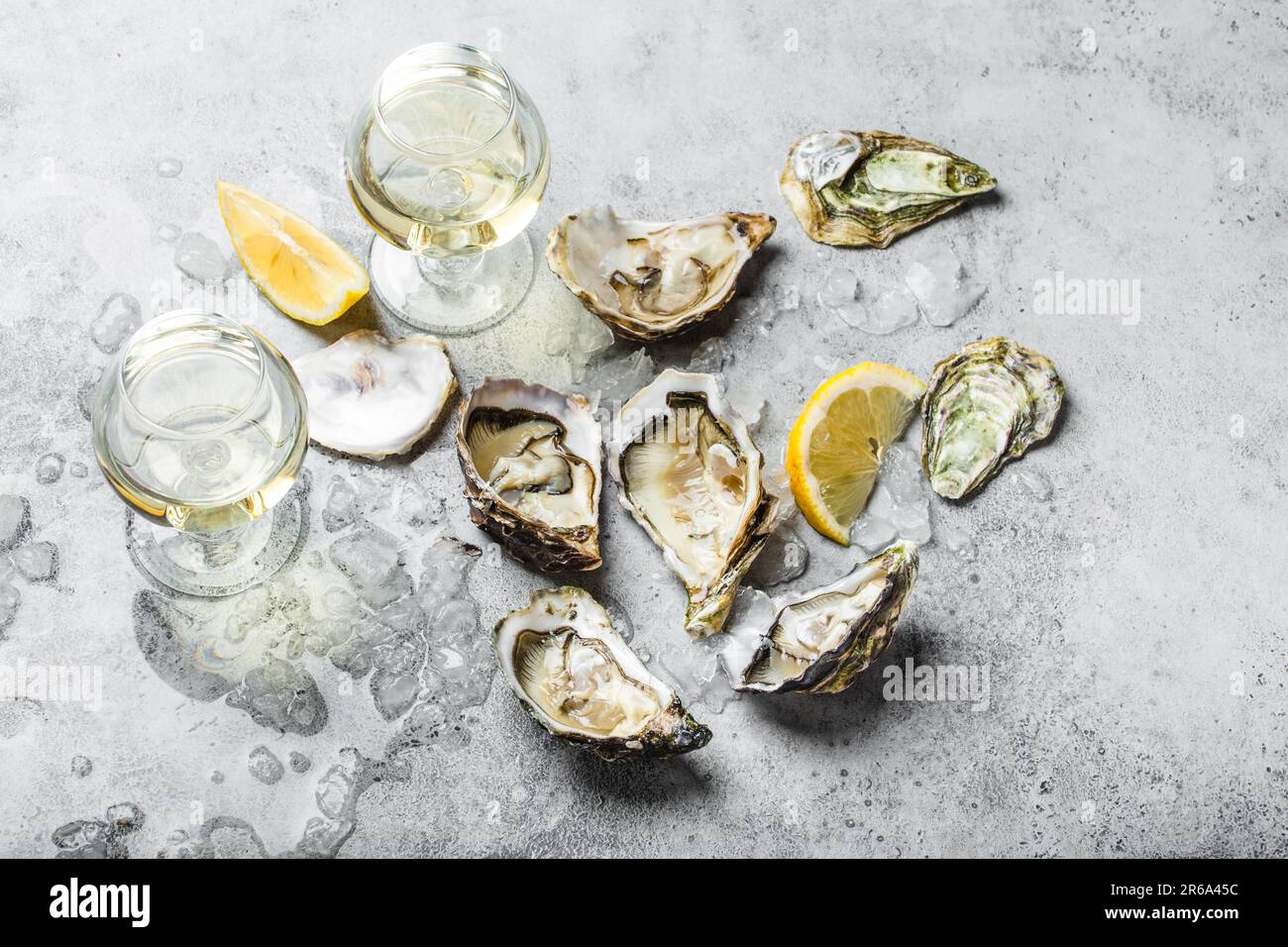 Nahaufnahme von einem halben Dutzend frischer Austern und Muscheln mit Zitronenkeilen, zwei Gläsern Weißwein oder Champagner, Blick von oben, grauer rustikaler Beton Stockfoto