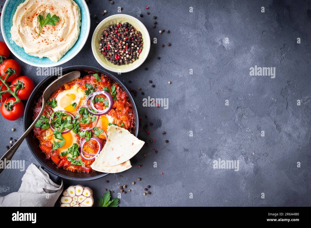 Shakshuka mit Pita-Brot in der Pfanne, Hummus in der Schüssel auf rustikalem Hintergrund. Traditionelle Gerichte aus dem Mittleren Osten. Spiegeleier mit Gemüse. Draufsicht. Leerzeichen Stockfoto