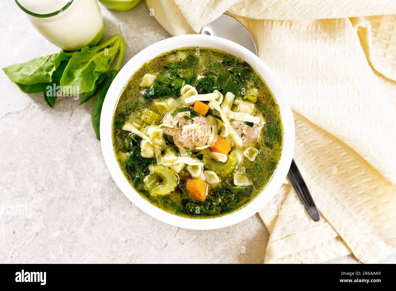 Italienische Suppe Ministra Maritata mit Fleischbällchen, Spinat, Karotten, Petiolsellerie und feiner Pasta in einer Schüssel, Serviette und Löffel gegen eine Granittheke Stockfoto