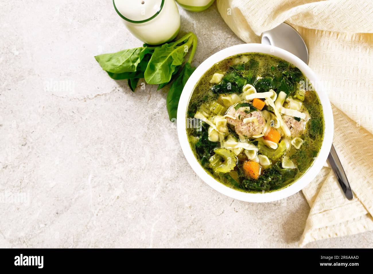 Italienische Suppe Ministra Maritata mit Fleischbällchen, Spinat, Karotten, Petiolensellerie und feiner Pasta in einer Schüssel, Serviette und einem Löffel auf einem Hintergrund aus Stein-Ta Stockfoto