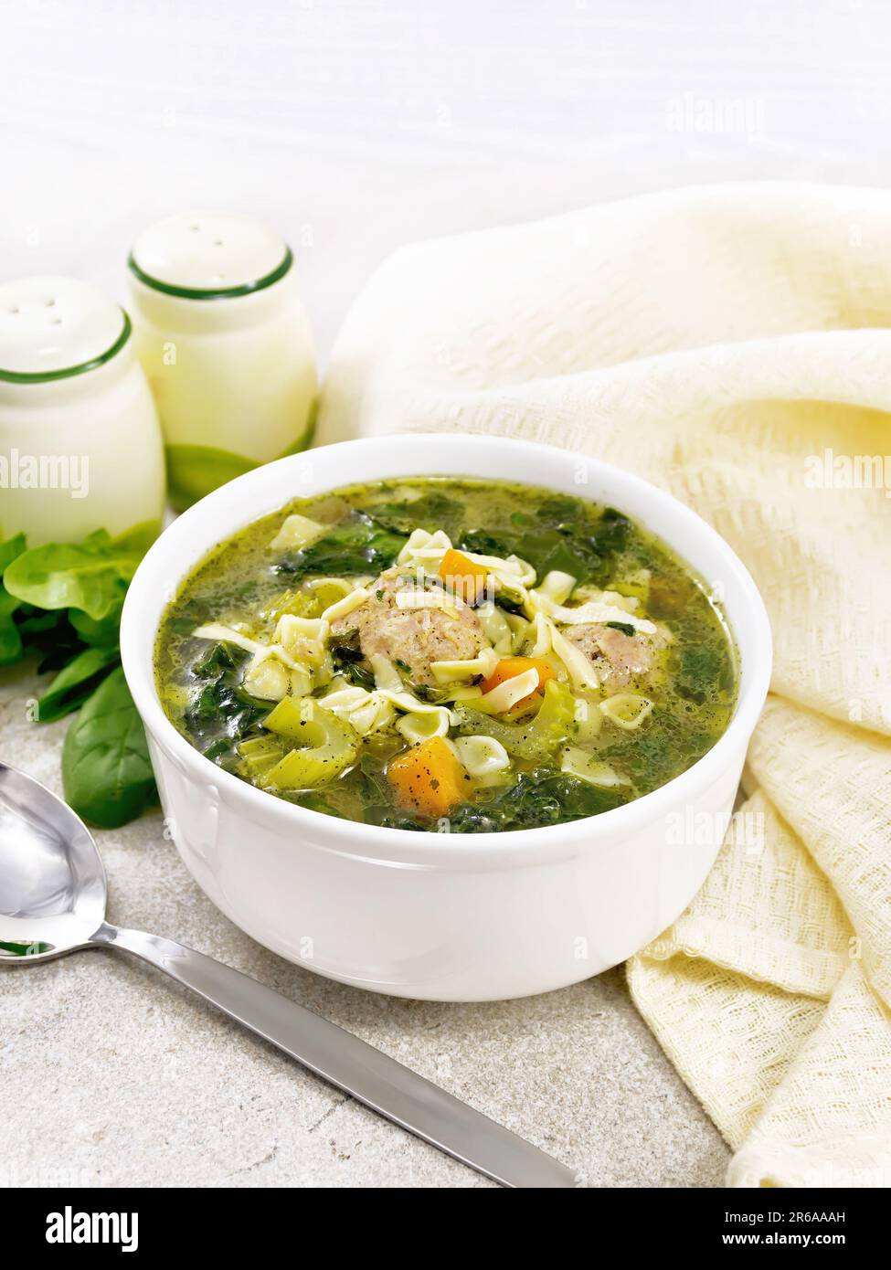 Italienische Suppe Ministra Maritata mit Fleischbällchen, Spinat, Karotten, Petiolensellerie und feinen Pasta in einer Schüssel, Serviette und Löffel auf einem Steintisch Stockfoto