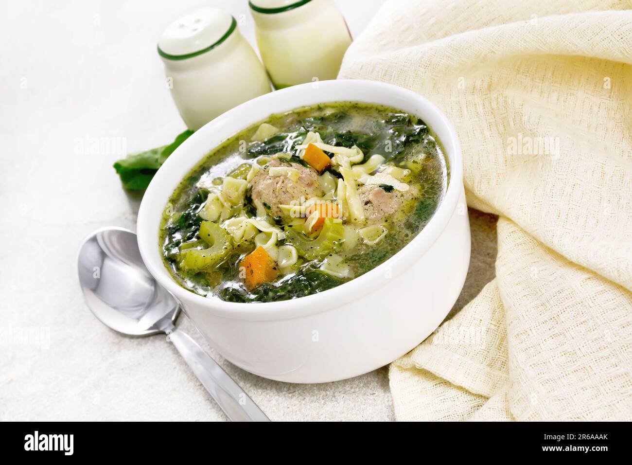 Italienische Suppe Ministra Maritata mit Fleischbällchen, Spinat, Karotten, Petiolsellerie und feiner Pasta in einer Schüssel, Serviette und einem Löffel auf einer Granittheke Stockfoto