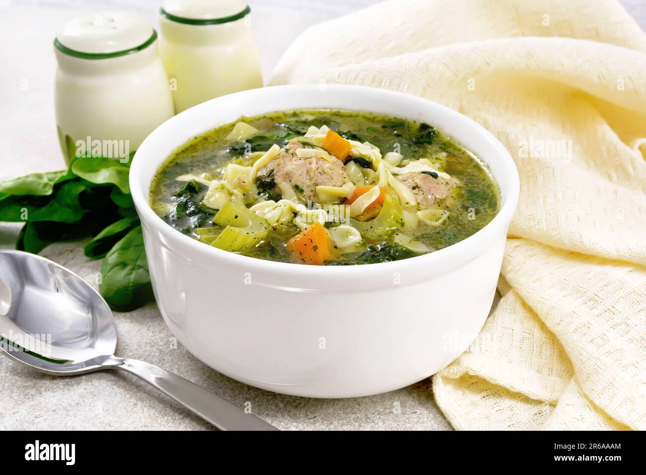 Italienische Suppe Ministra Maritata mit Fleischbällchen, Spinat, Karotten, Petiolsellerie und feiner Pasta in einer Schüssel, Serviette und einem Löffel am Granittisch Stockfoto