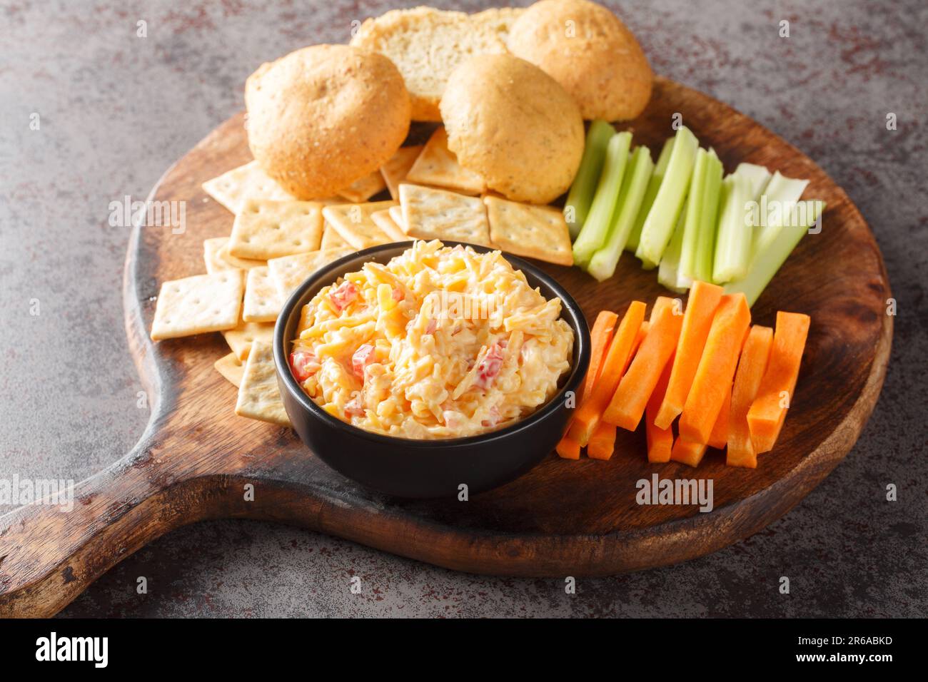 Hausgemachtes Pimento-Käsedip mit Karotten, Sellerie und Crackern, Seitenansicht auf dem Holzbrett auf dem Tisch. Horizontal Stockfoto