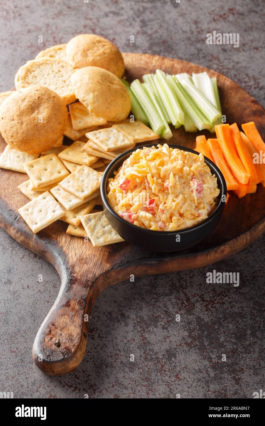 Hausgemachter Pimento-Käse mit Crackern und Gemüse auf dem Holzbrett auf dem Tisch. Vertikal Stockfoto