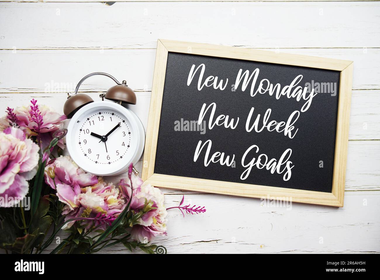 Neuer Montag, Neue Woche, Neue Ziele Textnachricht mit Weckruf und Blumendekoration auf Holzhintergrund Stockfoto