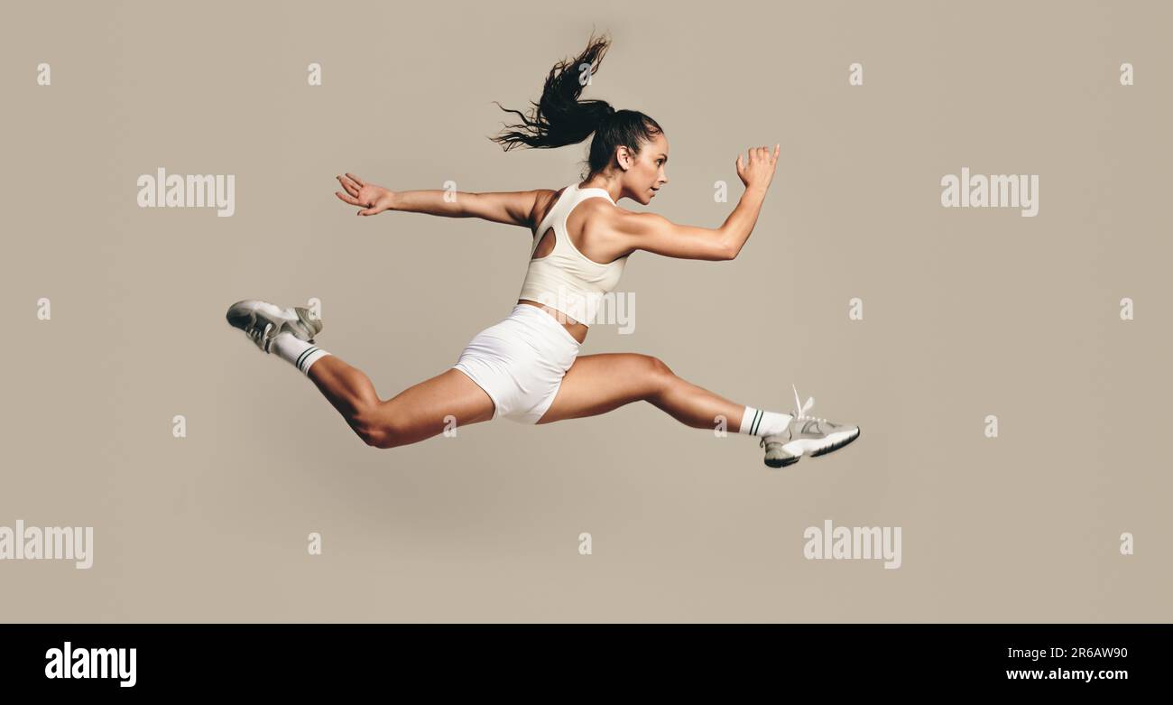 Aktive Sportlerin, die mitten in der Luft läuft und in einem Studio trainiert. Sportlerin kombiniert Kraft- und Kardio-Übungen für bessere Fitness und Stockfoto