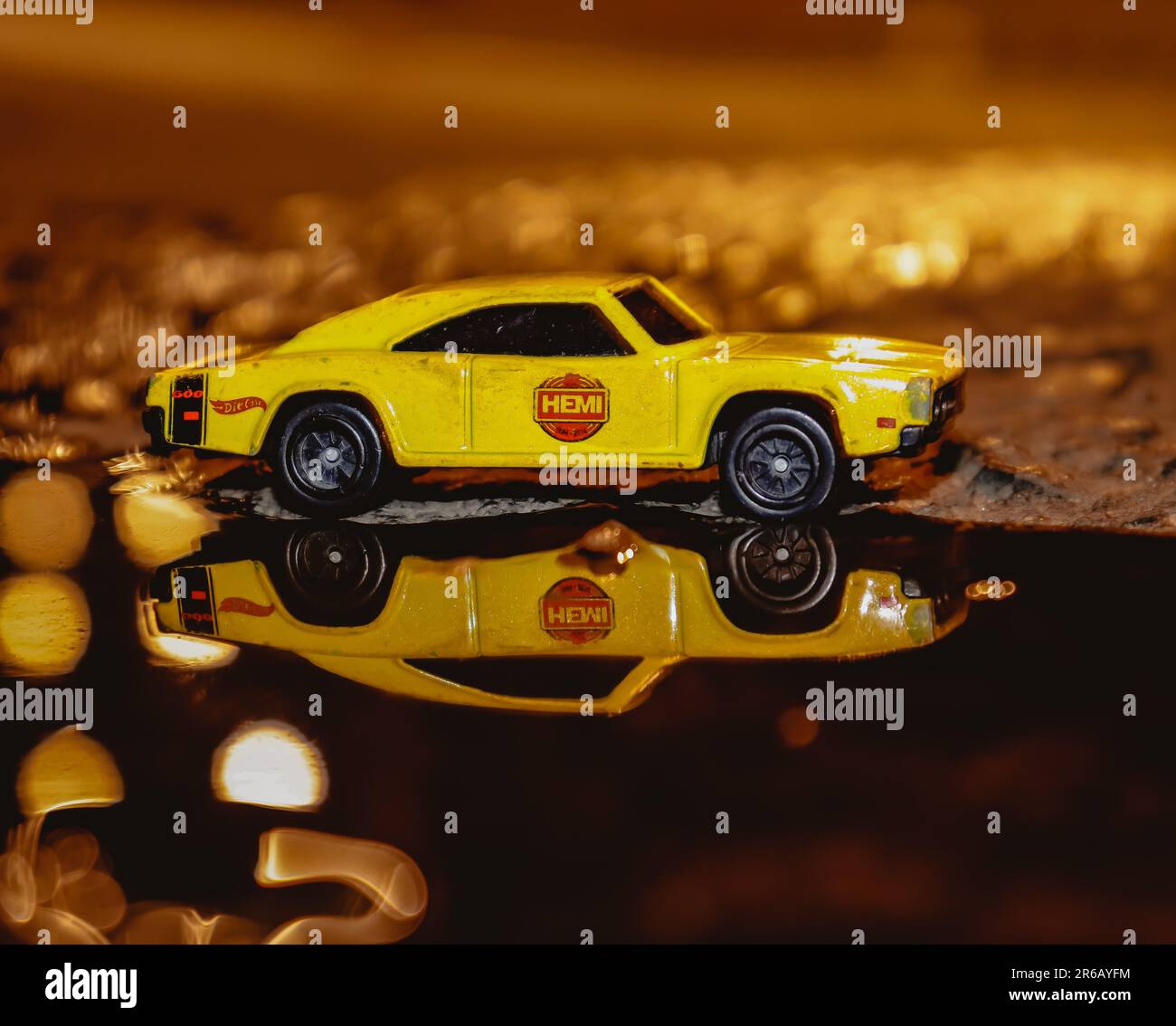 Nahaufnahme eines gelben Spielzeugautos aus Plastik vor einer reflektierenden Oberfläche mit mehreren Münzen, die um die Basis verstreut sind Stockfoto