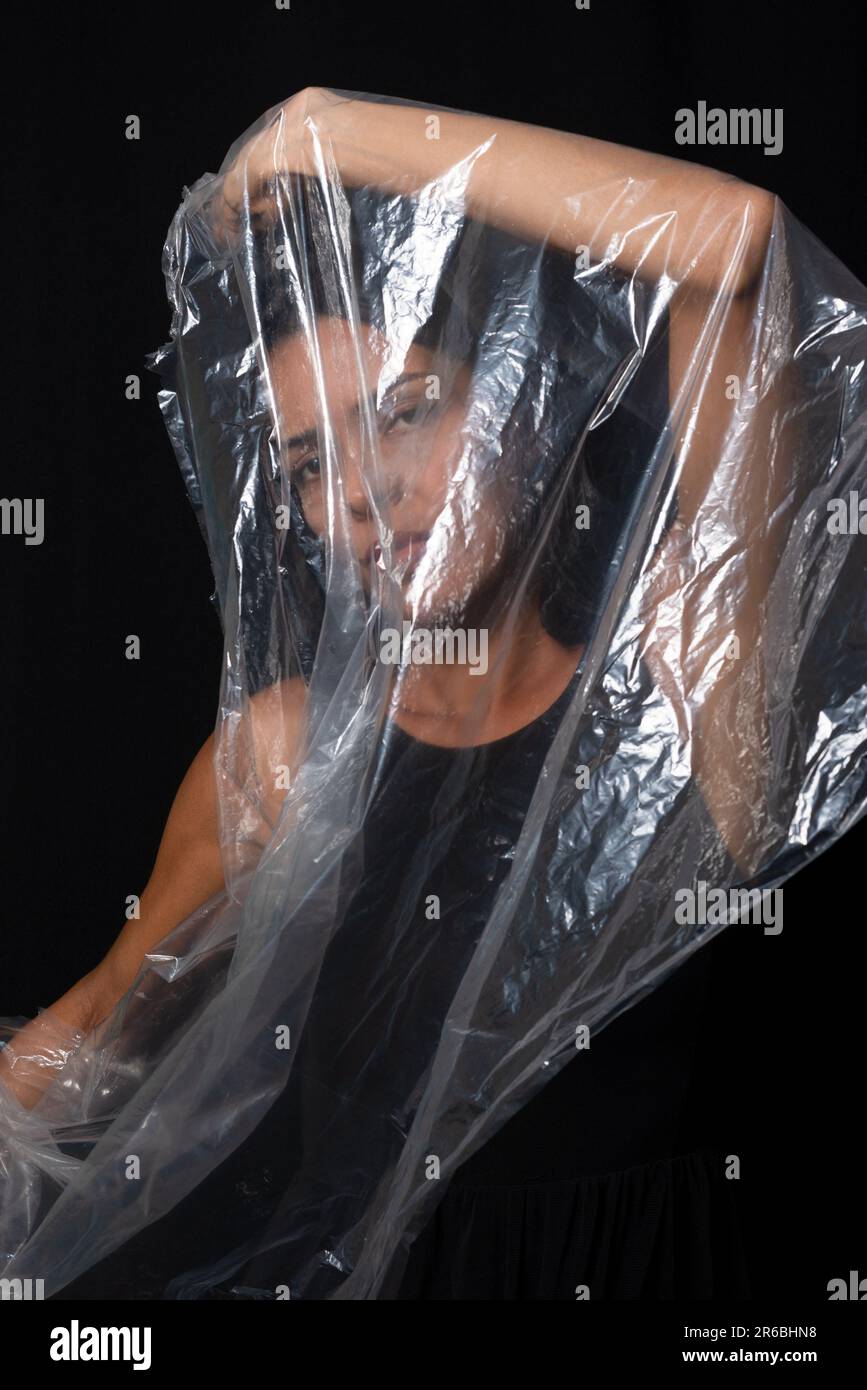 Eine Frau mit einer Plastiktüte über dem Kopf. Protest gegen die Verwendung von Plastik in der Welt. Umweltprobleme. Isoliert auf schwarzem Hintergrund. Stockfoto