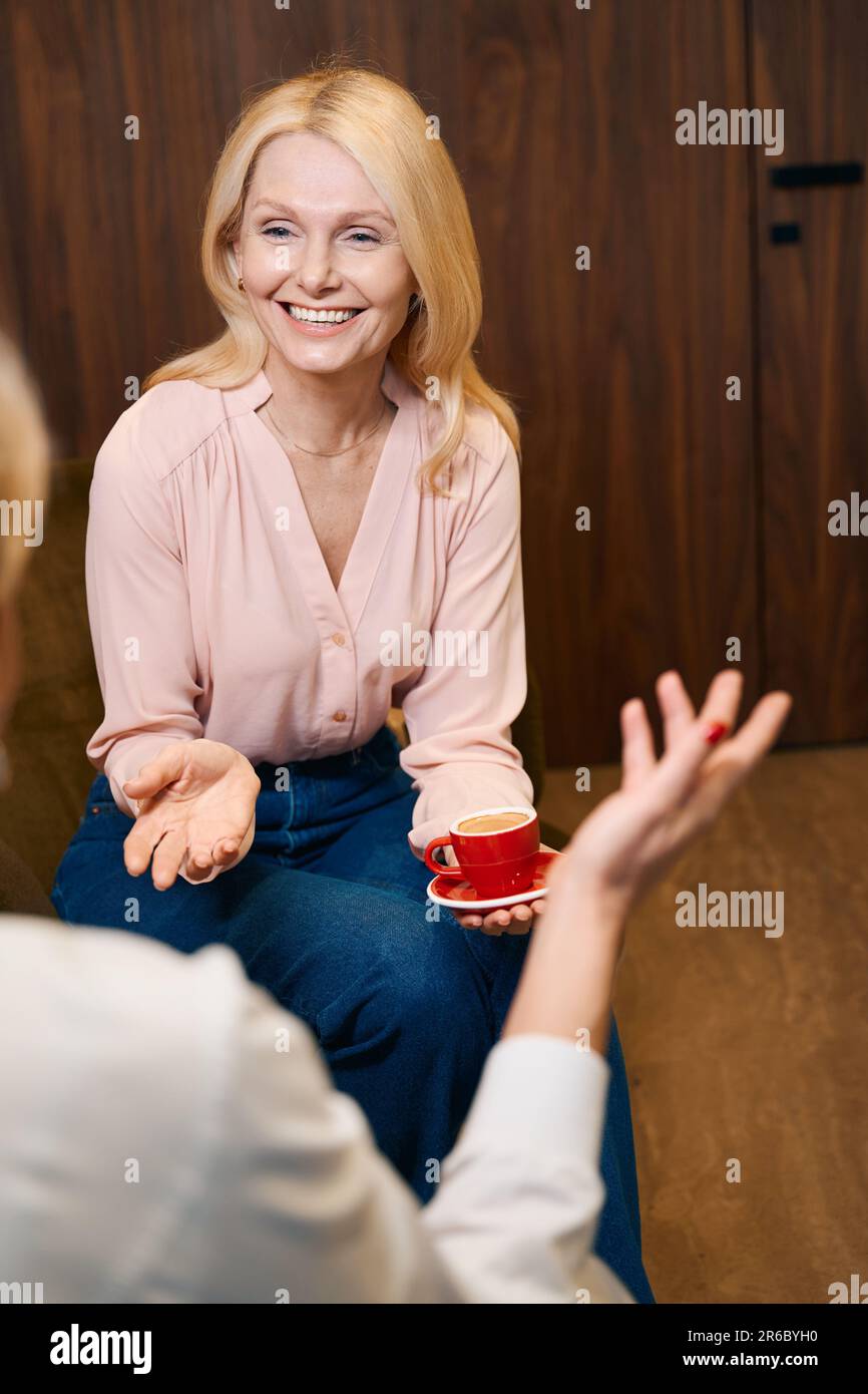 Eine Frau mit einer Tasse Kaffee, die lächelt und mit dem Arzt spricht Stockfoto