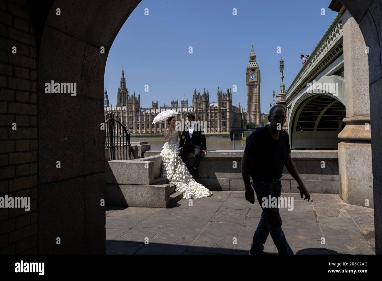 Chinesische frisch Verheiratete, sitzen Sie entlang der Mauer am Ufer der Themse mit Blick auf die Houses of Parliament, während Sie ein Foto an einem schlechten Sommertag in Großbritannien machen. Stockfoto