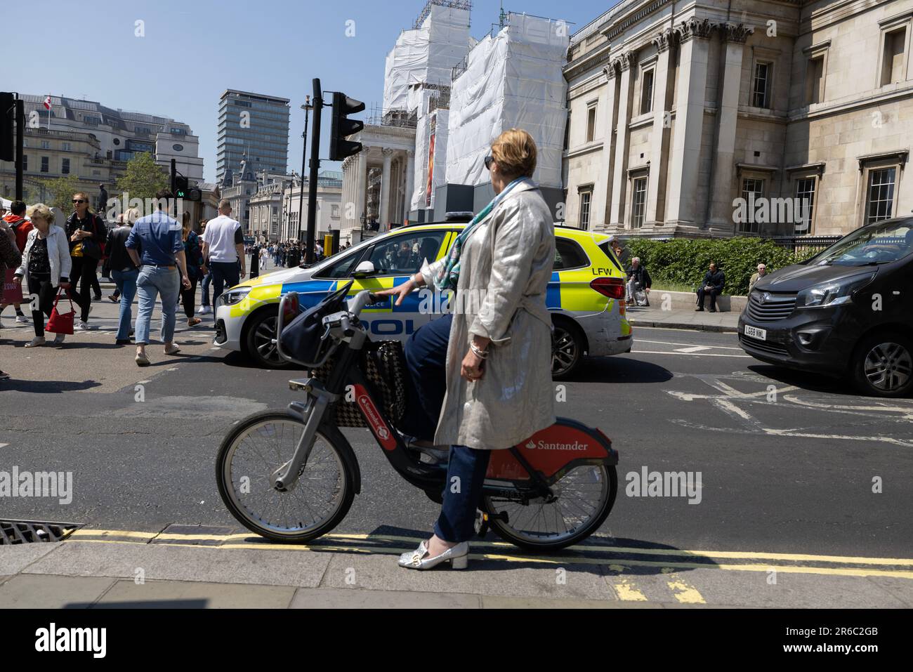 Frau mit Regenmantel auf Santander Bike, Charing Cross, West End von London an einem heißen Sommertag während einer Mini-Hitzewelle im Juni 2023, London, England, UK Stockfoto