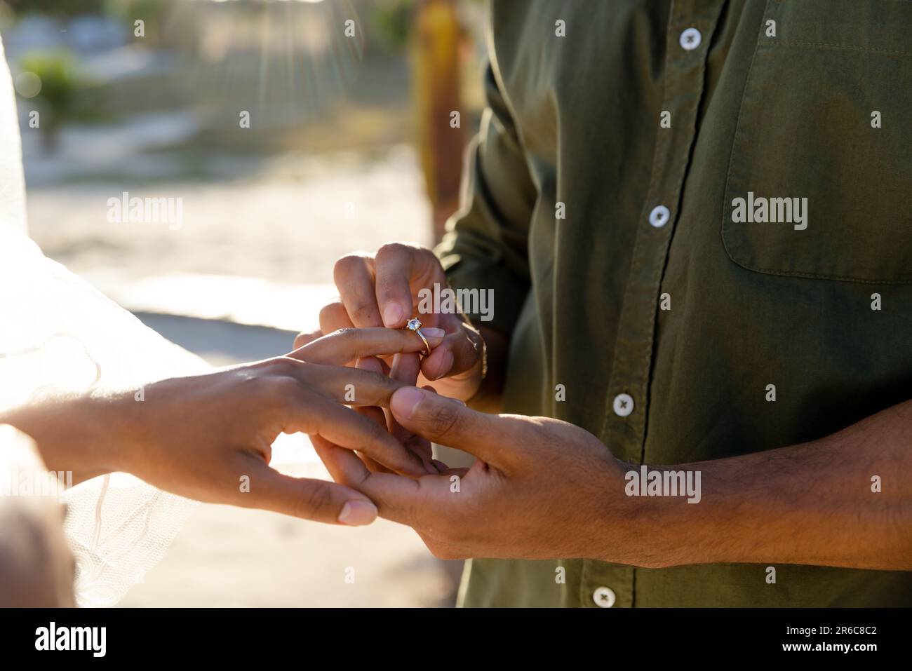 Die Mitte eines jungen, kaukasischen Bräutigams, der bei der Hochzeitszeremonie am Strand Ehering zur Braut trägt Stockfoto