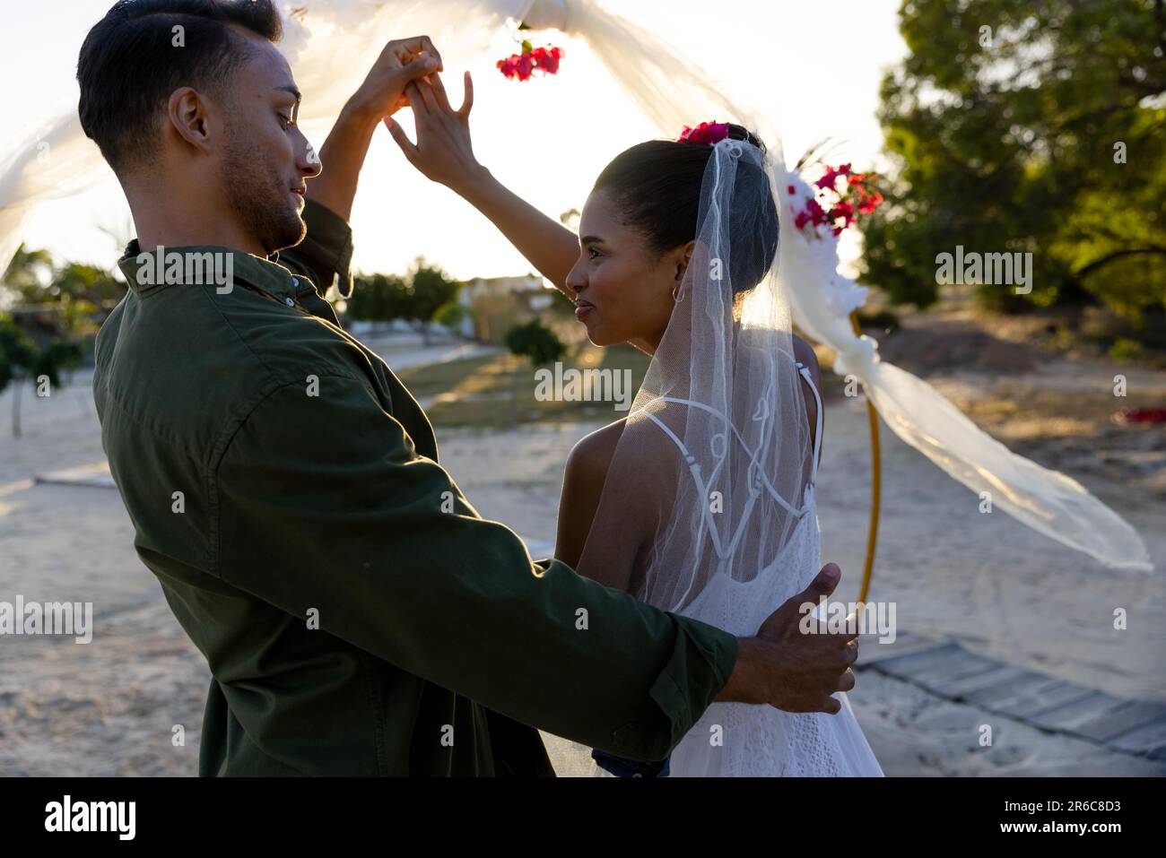 Kaukasisches, glückliches junges Paar, das bei der Hochzeitszeremonie bei Sonnenuntergang am Strand tanzt Stockfoto