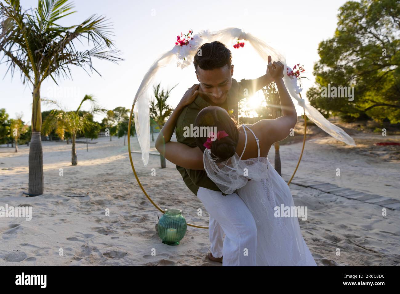 Kaukasisches frisch verheiratetes Paar tanzt romantisch bei der Hochzeitszeremonie am Strand bei Sonnenuntergang Stockfoto