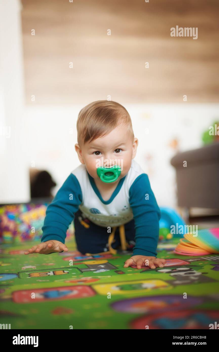 Porträt eines süßen, fröhlichen, lächelnden Jungen, der auf dem Hausboden krabbelt und in die Kamera schaut. Das Konzept von Freude und Glück. Vorderansicht. Liebe und Familiengefühle Stockfoto