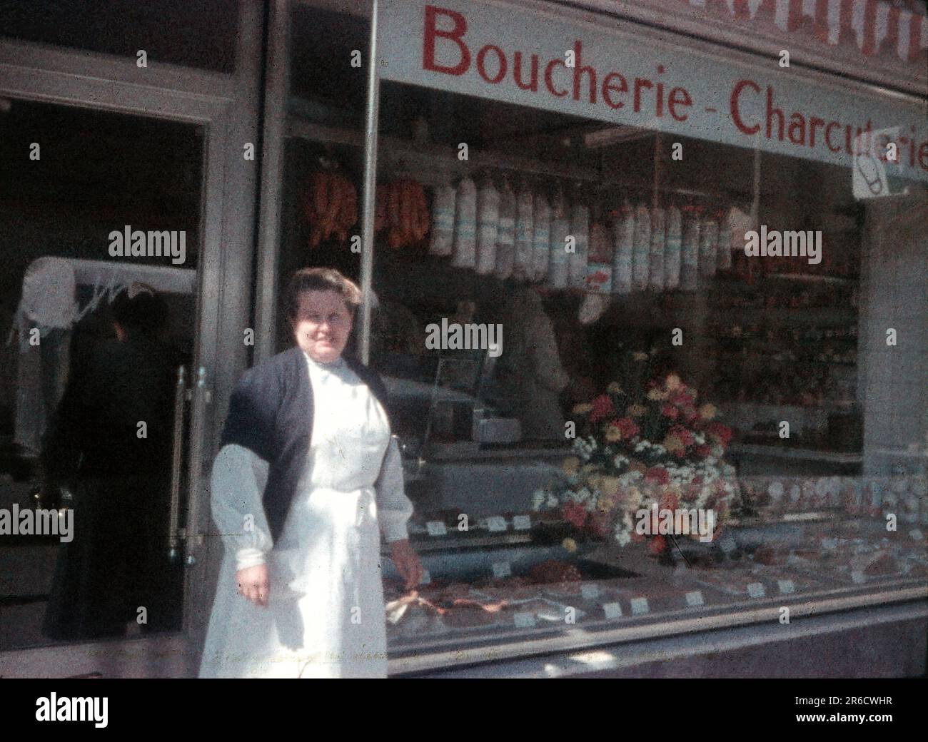 1950er Schweiz, eine Frau in weißer Schürze steht vor einem französischen Metzgerladen mit Fleisch im Fenster, Minox Subminiatur 8 mm Film Scan. Stockfoto 1950er Schweiz, eine Frau in weißer Schürze steht vor einem französischen Metzgerladen mit Fleisch im Fenster, Minox Subminiatur 8 mm Film Scan. Stockfoto