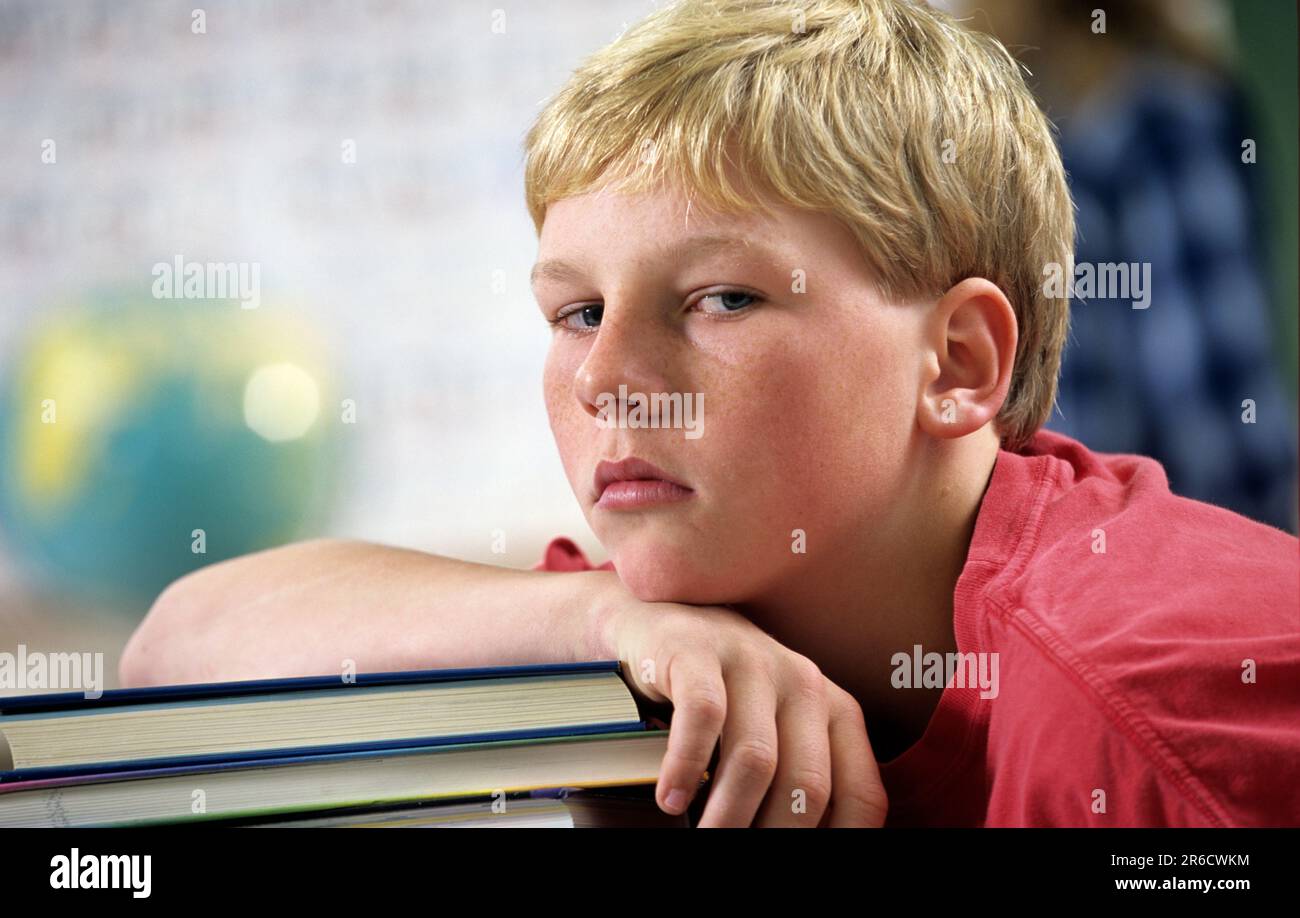 Ein abgenutzter Junge in der Schule, der im Unterricht nicht aufpasst, sich auf einen großen Stapel Bücher lehnt Stockfoto
