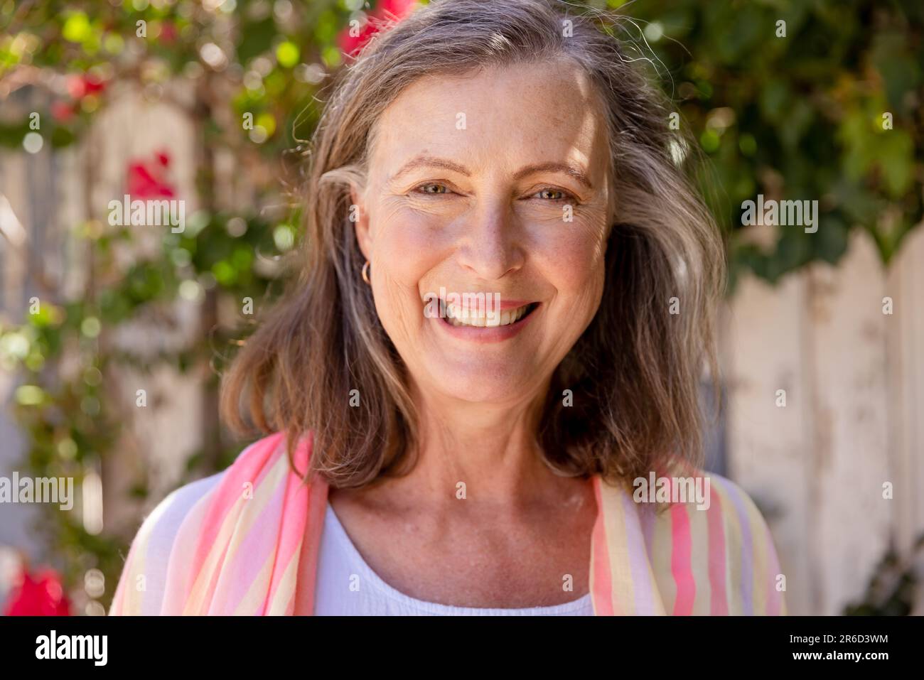 Nahaufnahme von einer schönen weissen Seniorin, die vor der Kamera lächelt, gegen Pflanzen, Kopierraum Stockfoto