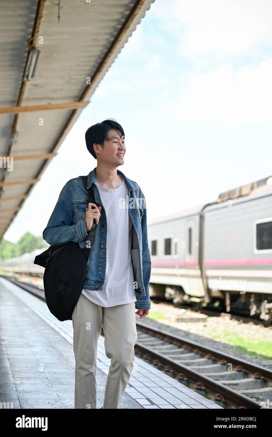 Porträt eines gutaussehenden und glücklichen jungen asiatischen Reisenden Rucksacktouristen mit seinem Rucksack, der am Bahnhof einen Zug erwischte. Urlaub, Transport Stockfoto