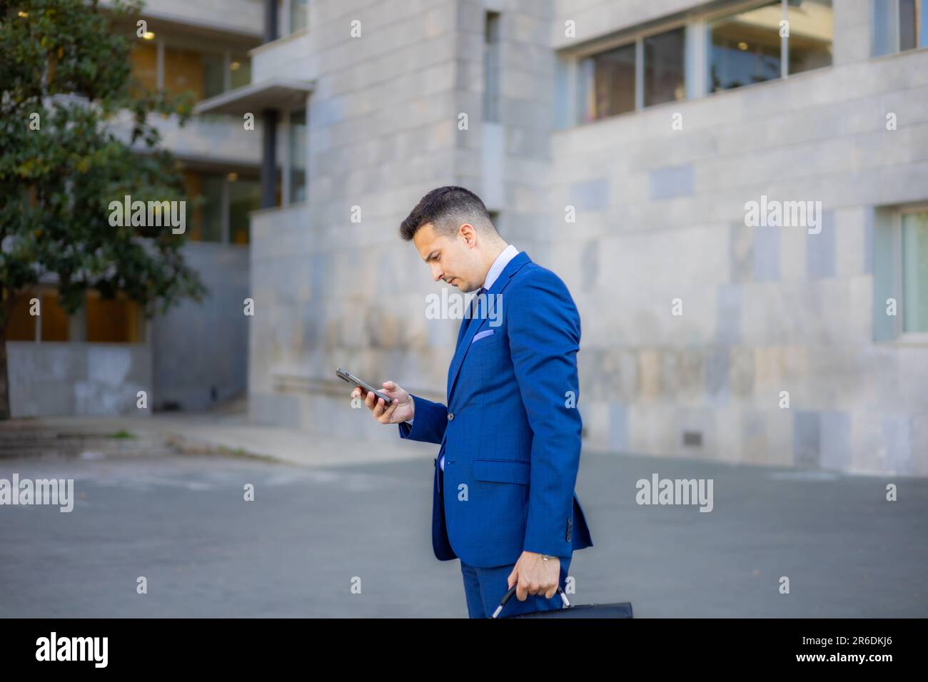 Attraktiver Ökonom, Anwalt, CEO, Unternehmer, Geschäftsführer und Geschäftsmann, der außerhalb des Büros mit dem Smartphone tippt. Stockfoto