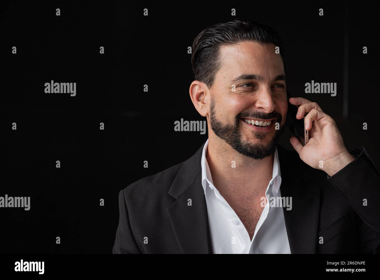 Porträt eines gutaussehenden Geschäftsmannes vor schwarzem Hintergrund, der am Telefon lächelt und spricht, in horizontaler Aufnahme Stockfoto