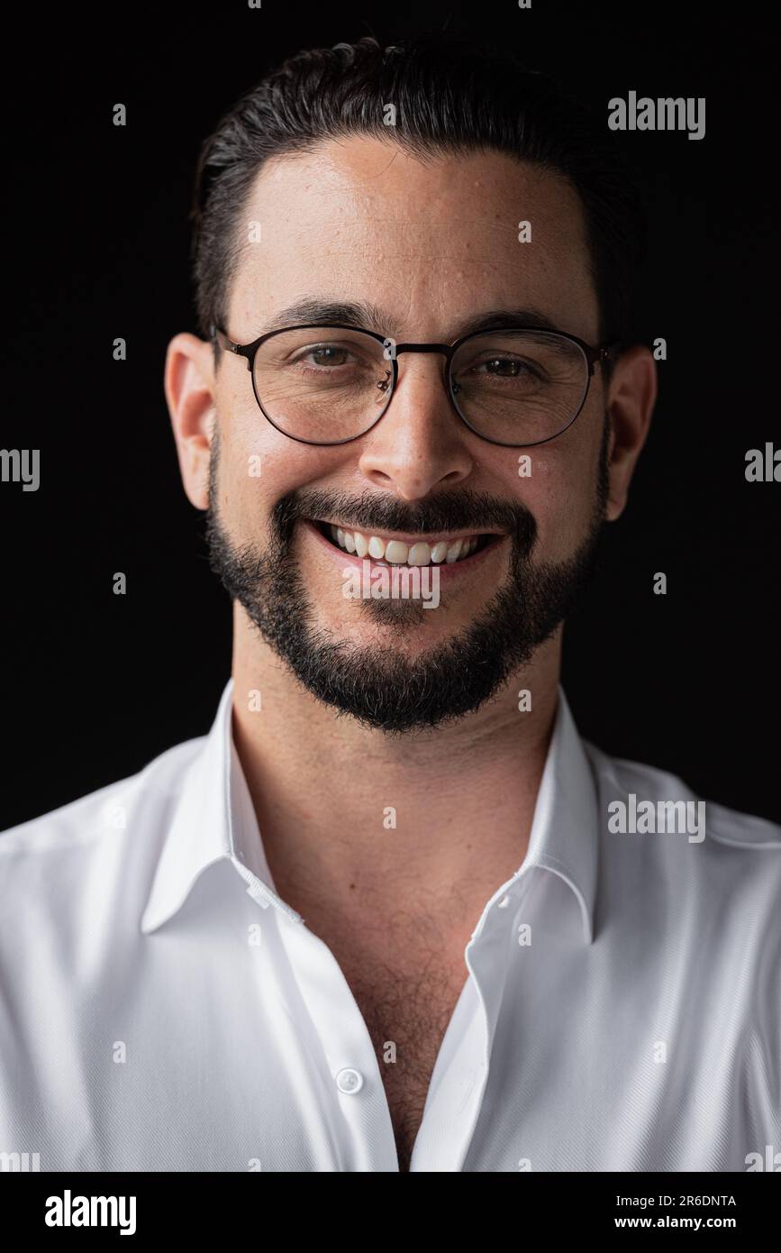 Porträt eines erfolgreichen Geschäftsmannes vor schwarzem Hintergrund, der eine Brille trägt und glücklich aussieht Stockfoto