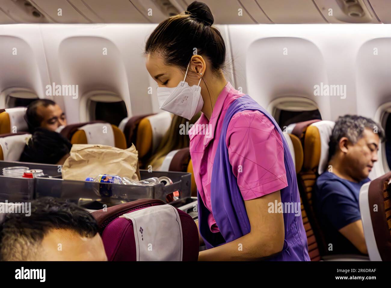 Thai Airways Kabinenpersonal mit Gesichtsmaske, das Passagiere im Economy-Bereich auf internationalen Flügen von Manila nach Bangkok bedient Stockfoto