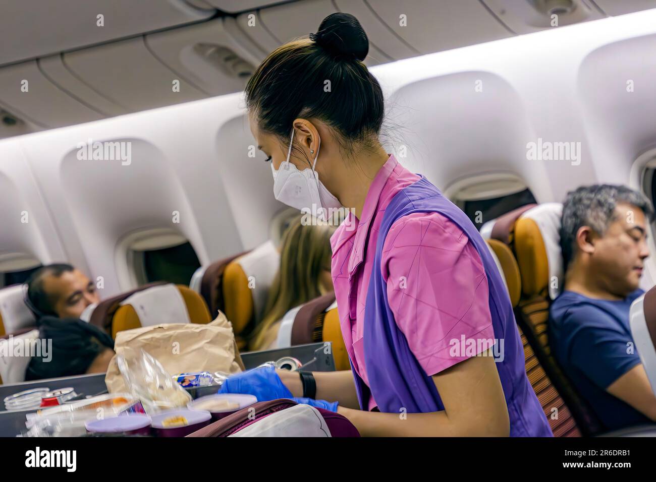 Thai Airways Kabinenpersonal mit Gesichtsmaske, das Passagiere im Economy-Bereich auf internationalen Flügen von Manila nach Bangkok bedient Stockfoto