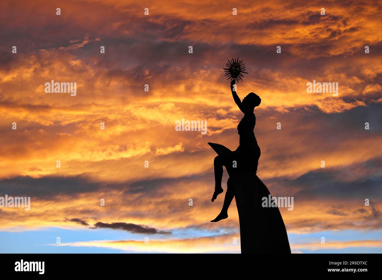 La silouette di una scultura contro un cielo pieno di nuvole dai colori ambrati al tramonto Stockfoto