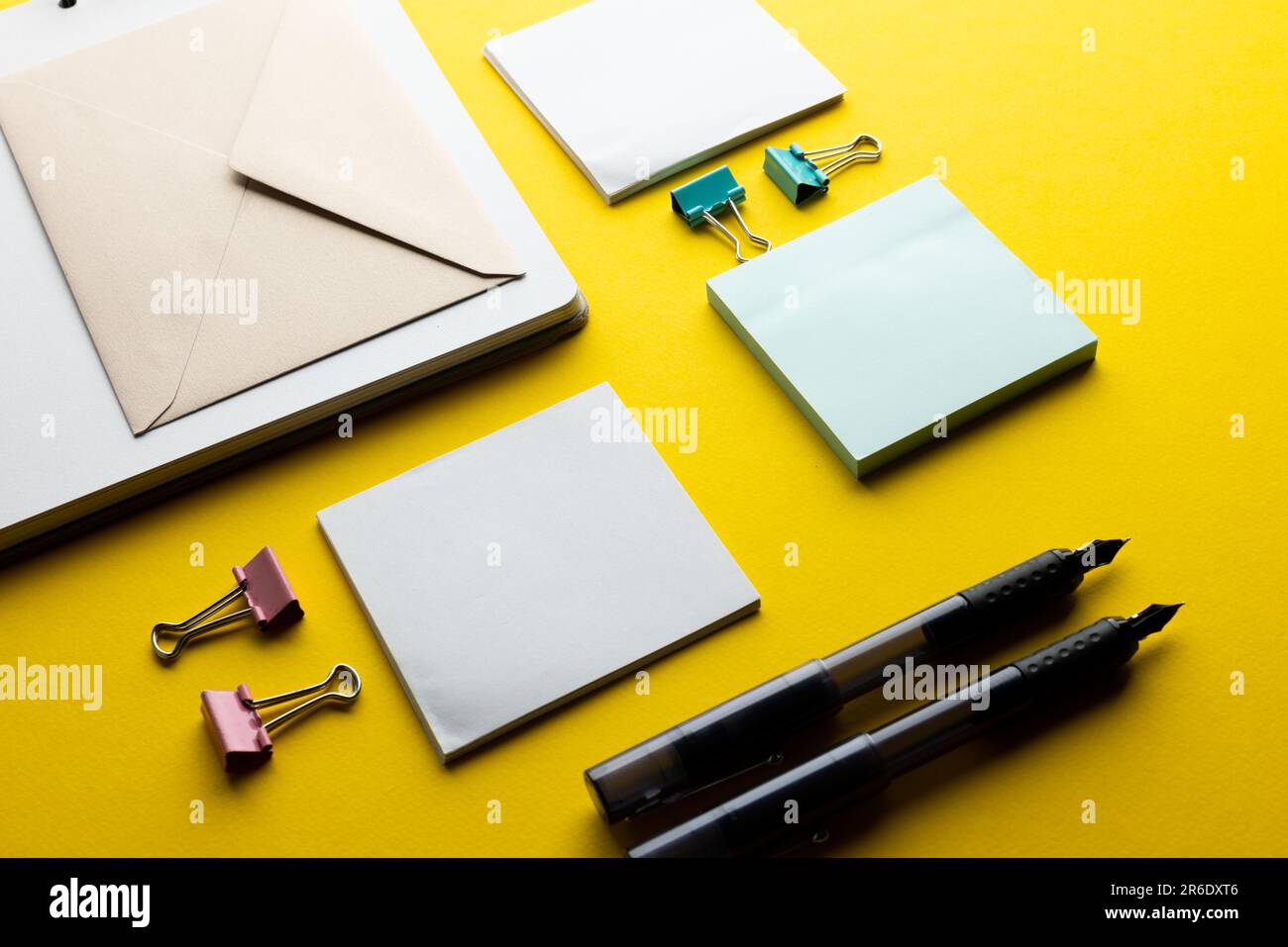 Flache Lage aus schwarzen Stiften, Umschlag und weißem Papier mit Kopierbereich auf gelbem Hintergrund. Schulmaterial, Schreiben, Malen, Zeichnen, Lernen, Schule Stockfoto