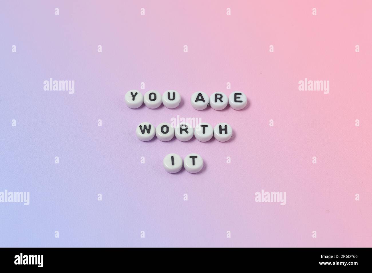 Draufsicht der Zitate „You're worth it“ aus Perlen auf pastellfarbenem Hintergrund. Motivation und Erfolgskonzept Stockfoto