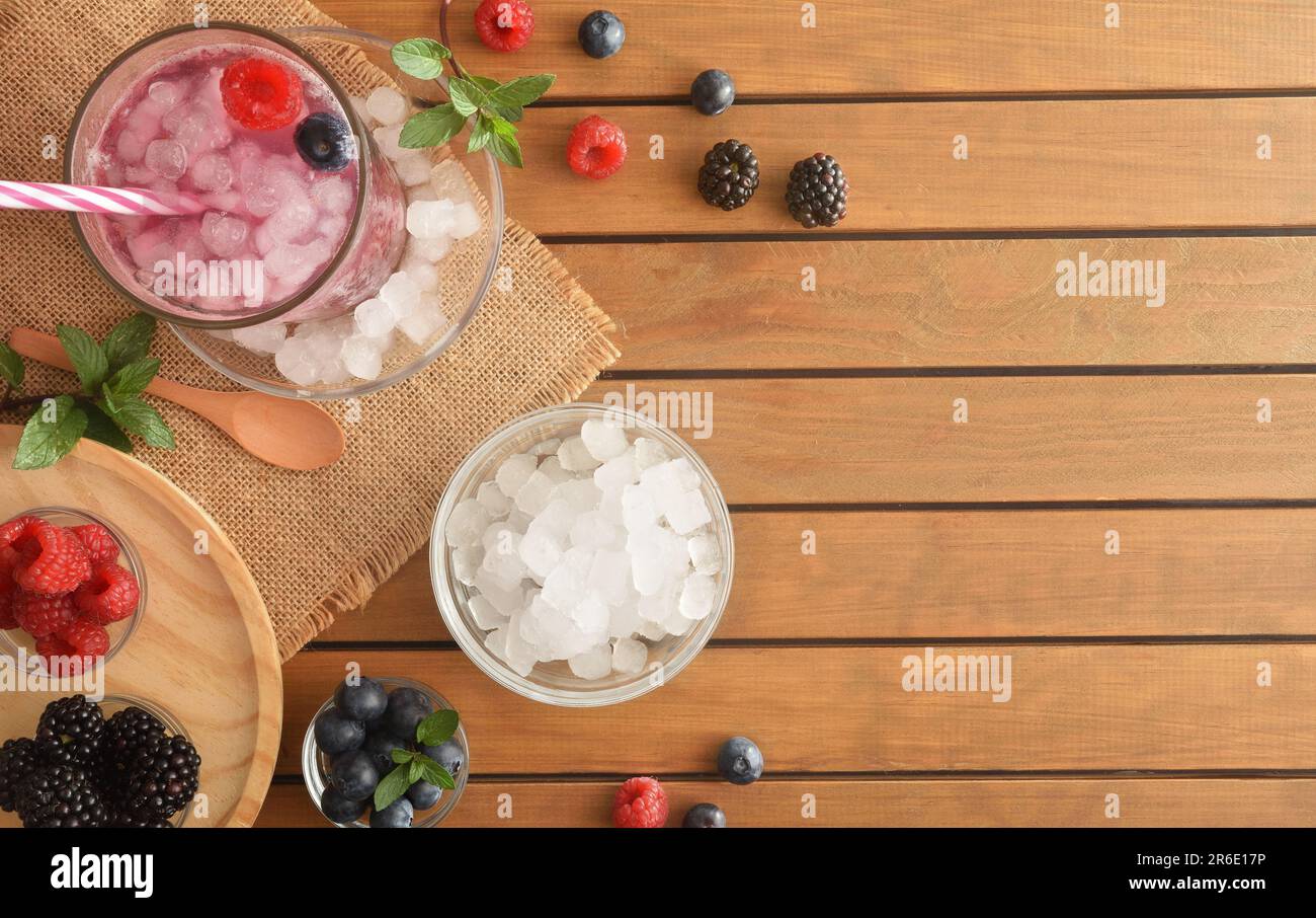 Hintergrund mit kaltem Waldfruchtgetränk mit Beeren und zerkleinertem Eis auf einem Holztisch. Draufsicht. Horizontale Zusammensetzung. Stockfoto