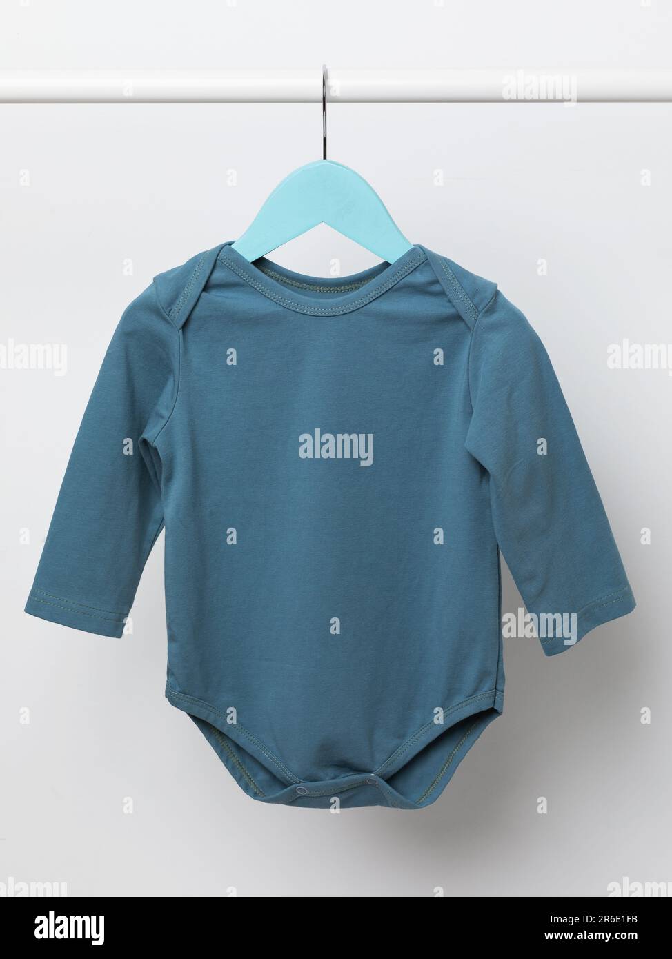Ein blauer langärmeliger Babyanzug hängt auf einem hellen Hintergrund an einem Kleiderbügel Stockfoto